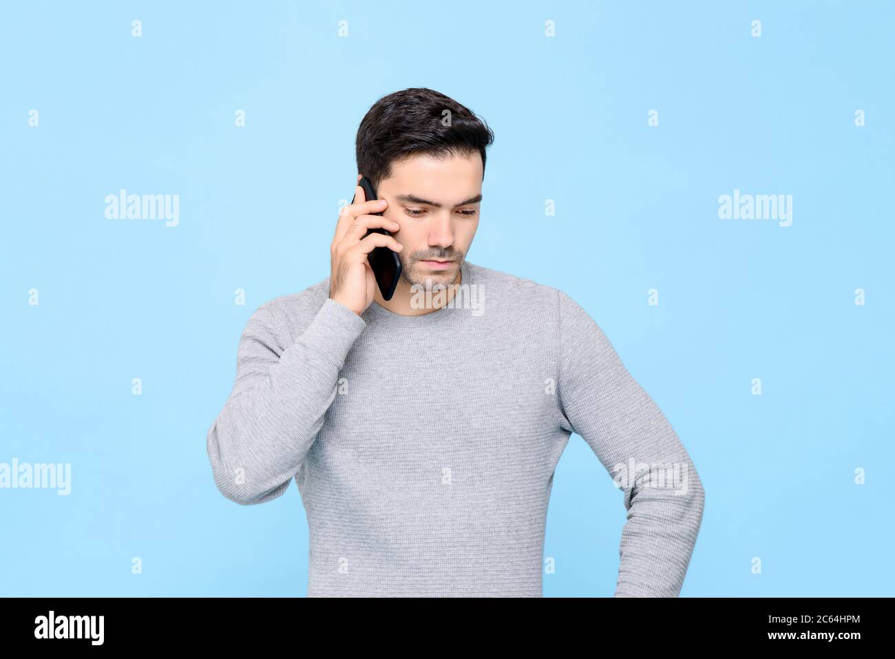 Portrait d'un homme caucasien sérieux et contrarié appelant sur un téléphone portable avec une expression faciale malheureuse dans un arrière-plan isolé de studio bleu Banque D'Images