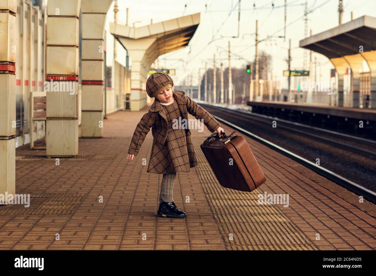 Belle charmante petite fille attendant le train à la gare tenant des bagages Banque D'Images