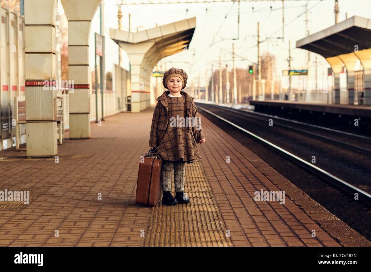 Belle charmante petite fille attendant le train à la gare tenant des bagages Banque D'Images