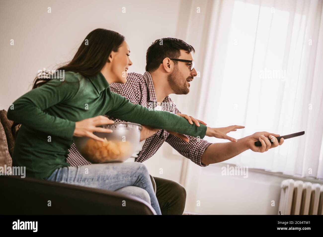 Les jeunes couples regardent la télévision à la maison. Ils font des querelles. Banque D'Images