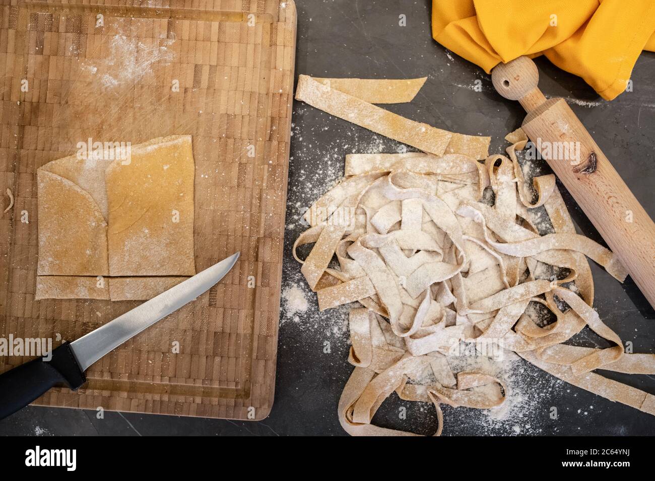 Gros plan à angle élevé de tagliatelle fraîchement confectionné, goupille élastique et couteau sur une planche à découper en bois. Banque D'Images