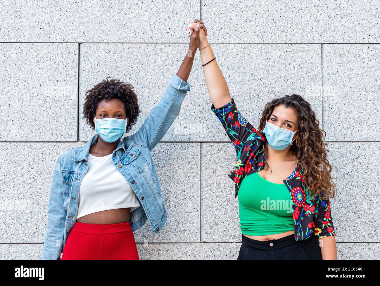 deux jeunes amies, une blanche et une noire, élèvent leurs poings ensemble comme un signe de fraternité et de protestation contre le racisme, une nouvelle socialisation Banque D'Images