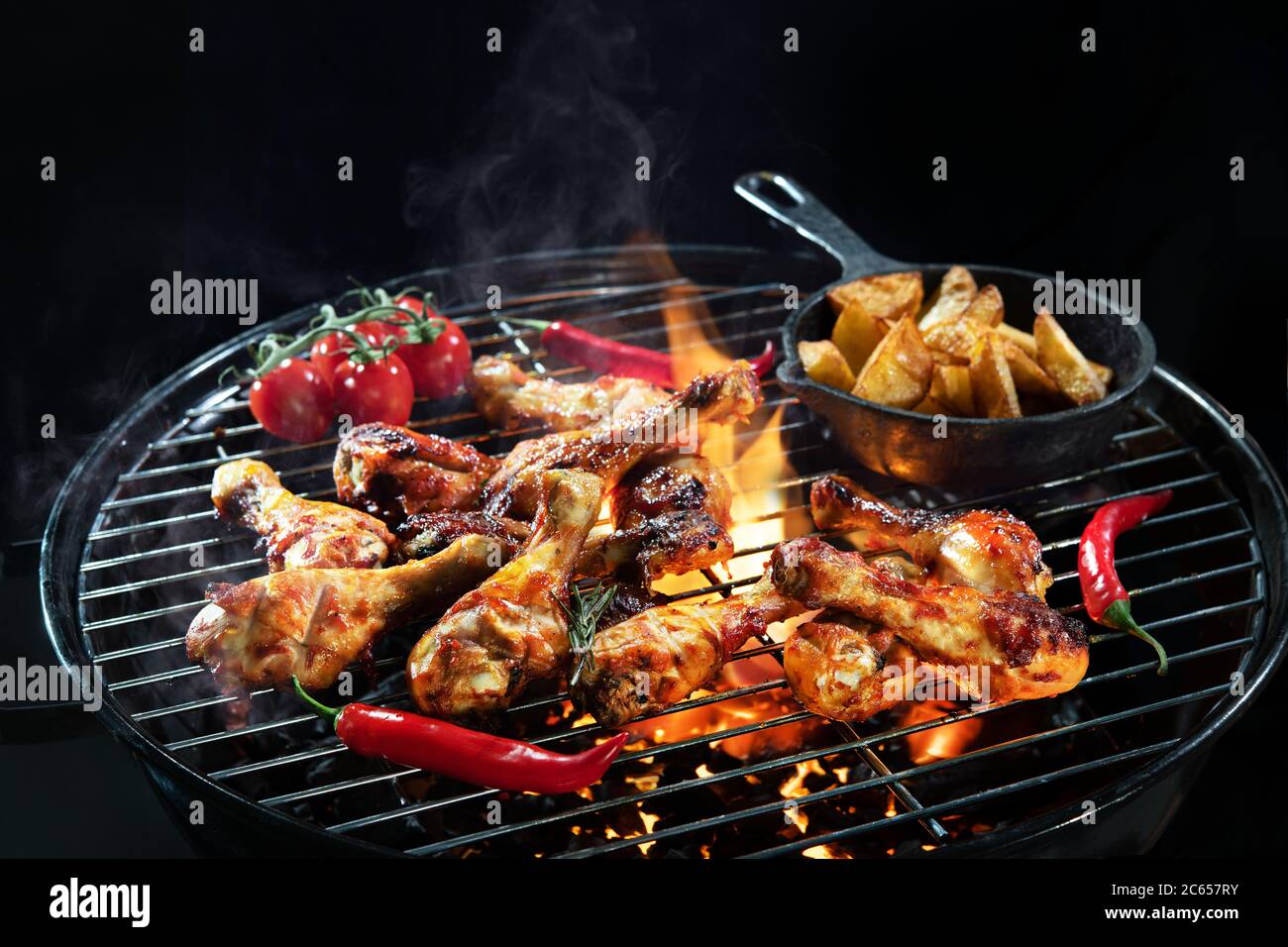 Des cuisses de poulet grillées ou des pilons de poulet sur le barbecue chaud flamboyant avec de la fumée sur fond sombre Banque D'Images