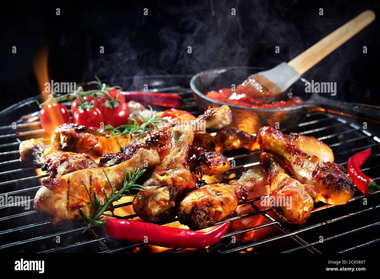 Des cuisses de poulet grillées ou des pilons de poulet sur le barbecue chaud flamboyant avec de la fumée sur fond sombre Banque D'Images