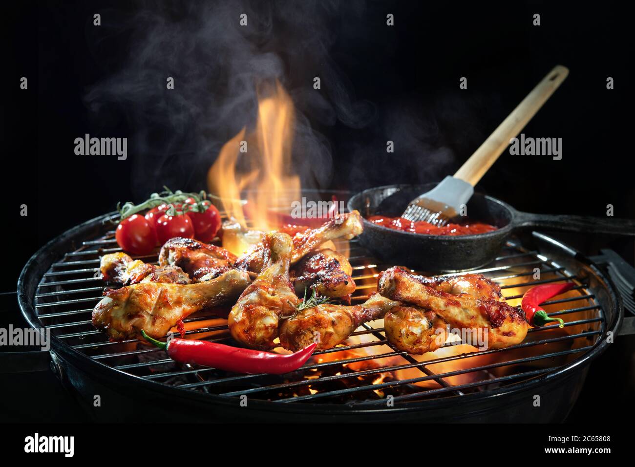 Des cuisses de poulet grillées ou des pilons de poulet sur le barbecue chaud flamboyant avec de la fumée sur fond sombre Banque D'Images