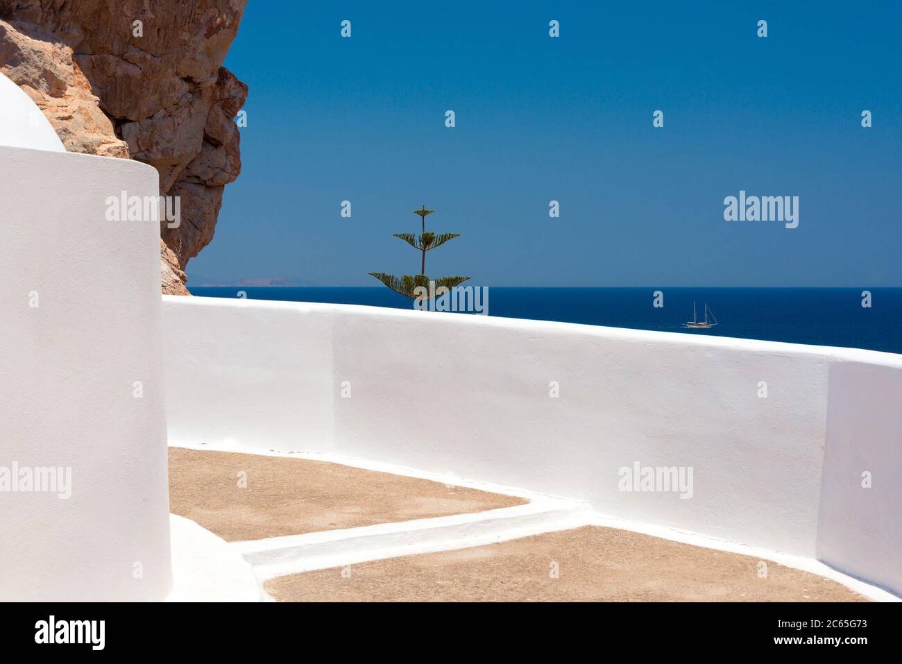 Un bateau s'étend au-delà du mur blanc de l'église Agios Ioannis, près de Monolithos, sur l'île de Santorin Banque D'Images