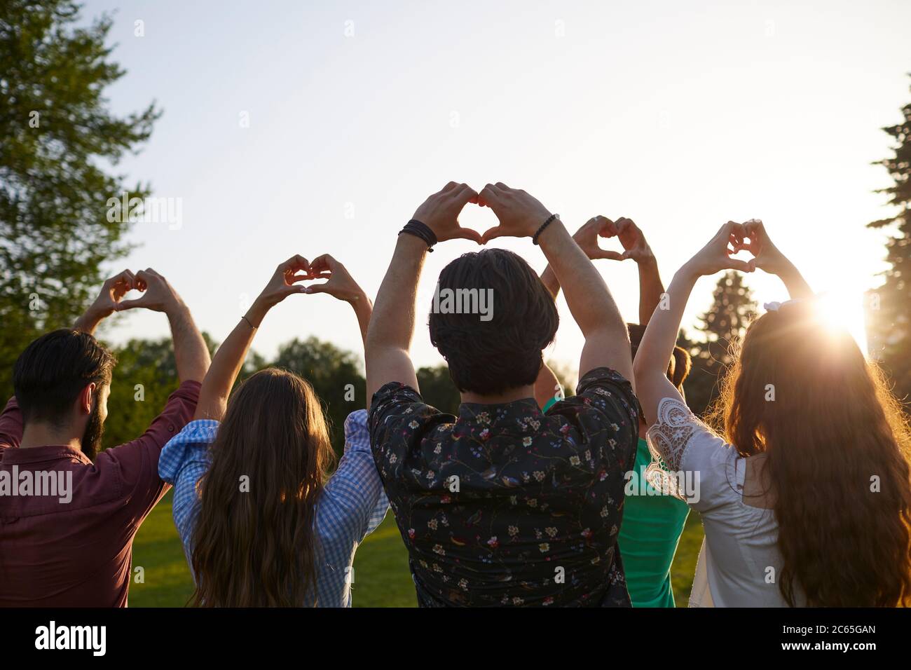 Signe main coeur. Un groupe de personnes tient les mains avec un signe de coeur sur un fond de ciel avec coucher de soleil sur la nature. Banque D'Images