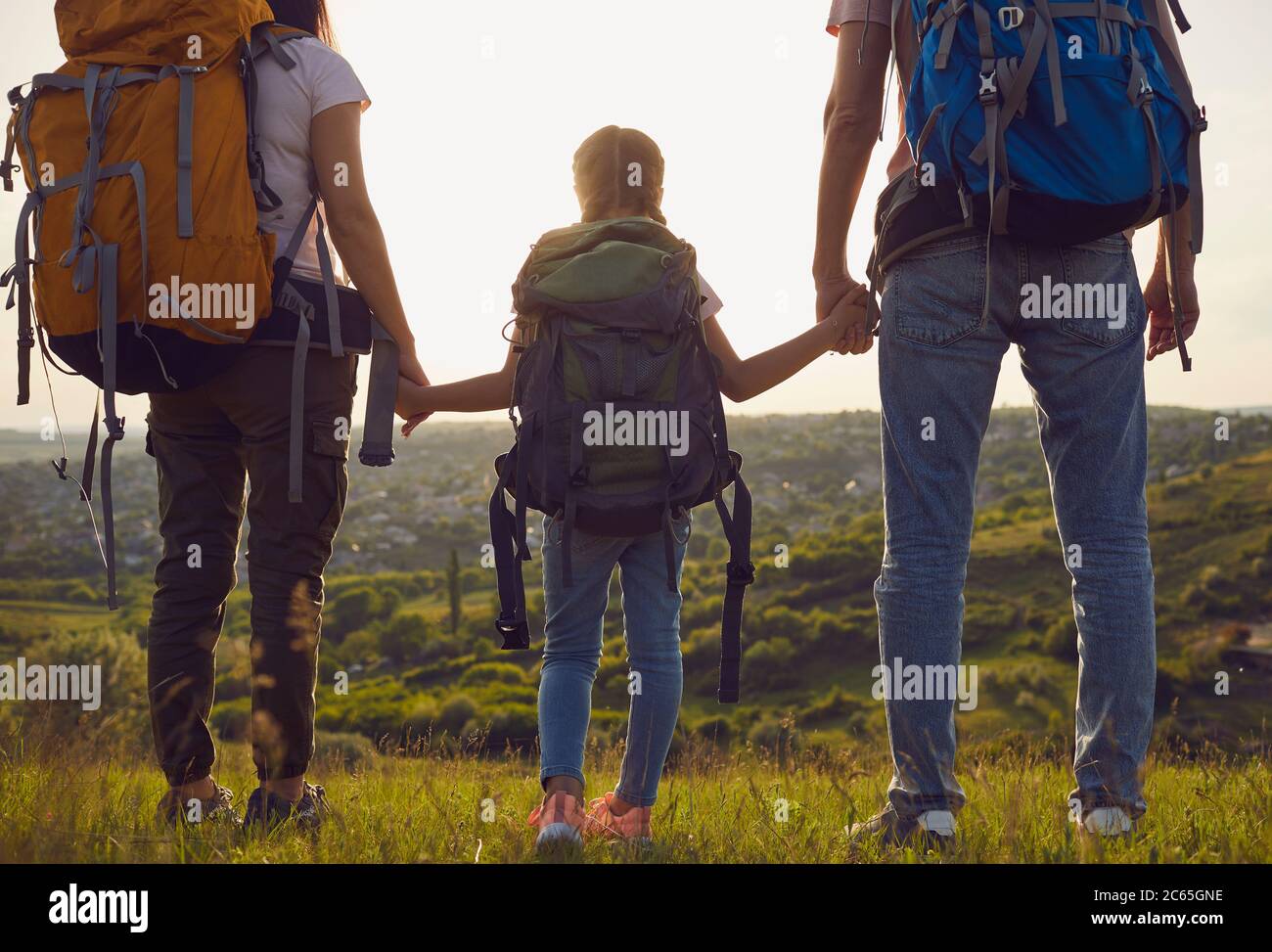 Famille heureuse avec des sacs à dos sur la nature au coucher du soleil. Randonnée pédestre concept de tourisme familial. Vue arrière. Banque D'Images