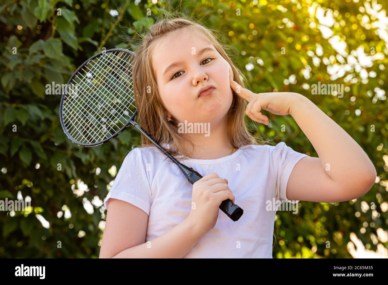 Une petite fille fait un visage glamour avec joie. Jolie petite fille jouant au badminton à l'extérieur le jour d'été chaud et ensoleillé. Banque D'Images