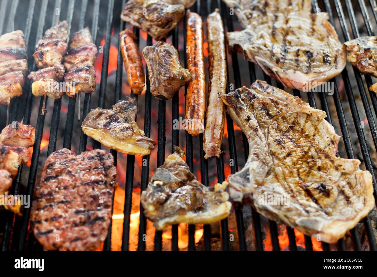 Assortiment de différentes viandes grillées sur un feu de barbecue sur les charbons chauds en gros plan plein cadre avec du bœuf, des saucisses et des brochettes Banque D'Images