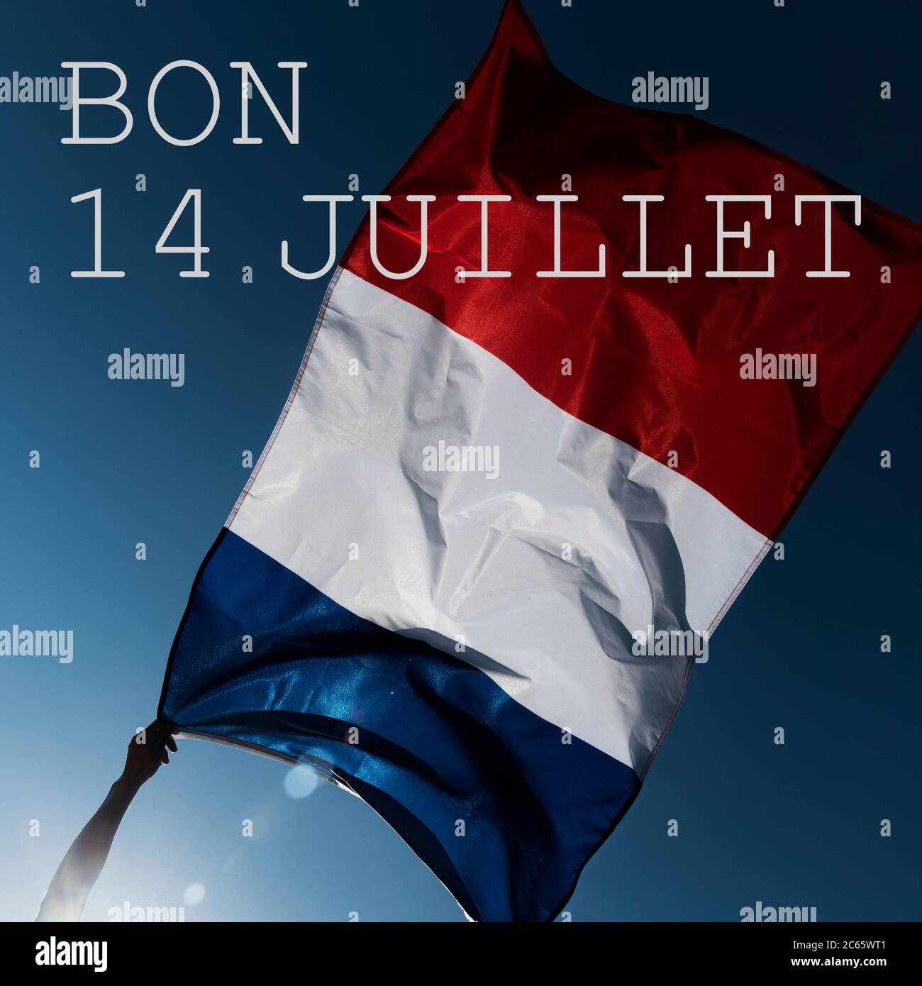 Homme portant un drapeau français agitant sur le vent et le texte bon 14 juillet, heureux 14 juillet, la journée nationale de la France écrite en français, contre le blu Banque D'Images