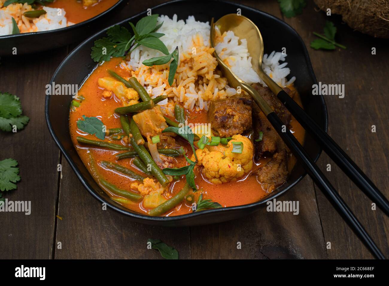 Curry rouge végétarien thaï avec du seitan, des haricots et du chou-fleur sur du riz, servi dans des bols noirs Banque D'Images