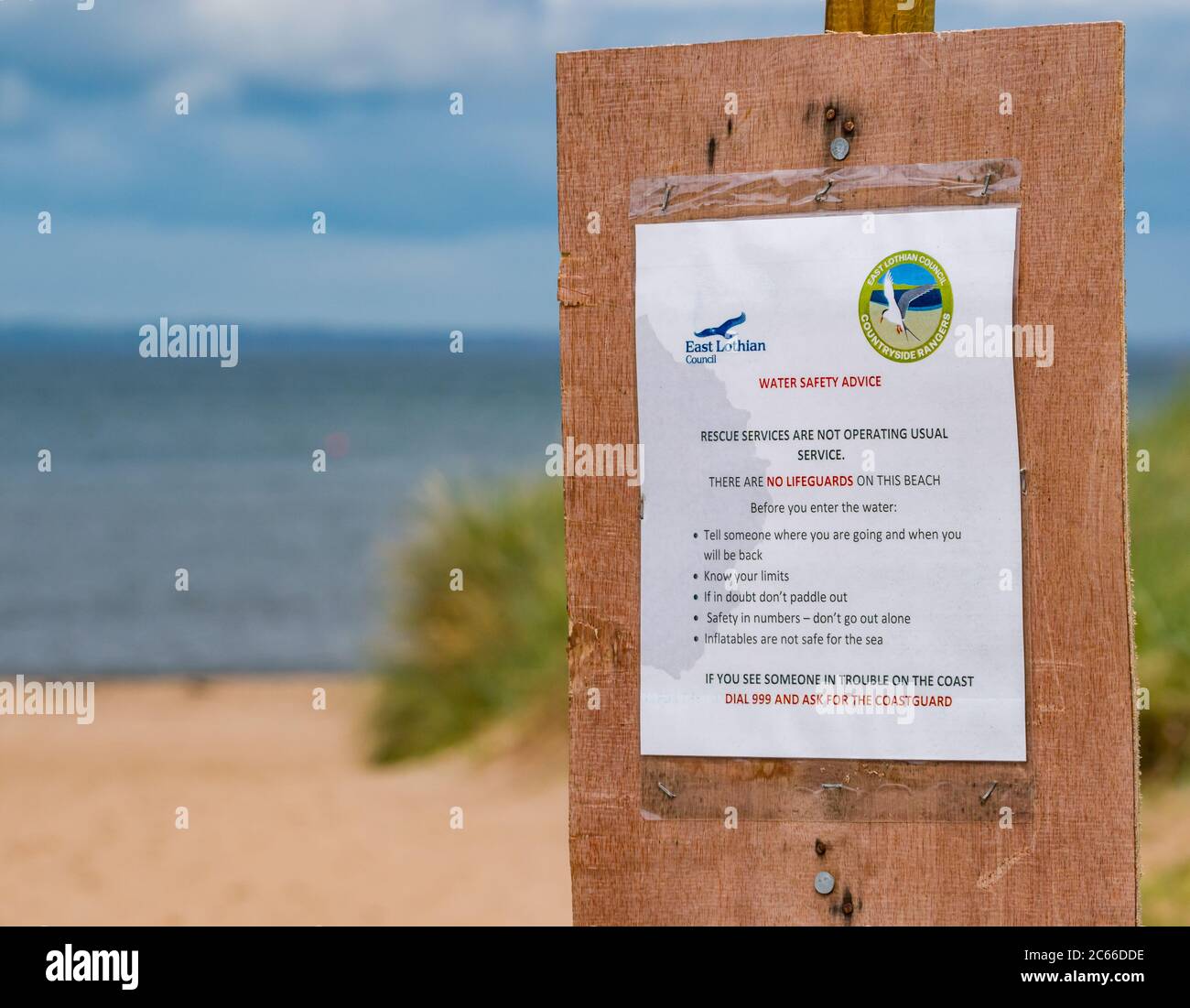 East Lothian, Écosse, Royaume-Uni, 7 juillet 2020. Météo au Royaume-Uni : les familles bénéficient du bref soleil sur la plage de Broad Sands Beach à Yellowcraig sur la côte du Firth of Forth maintenant que les parcs de stationnement du Conseil de Lothian est ouverts. Des mesures de distance sociale sont en place pour créer des itinéraires séparés vers et depuis la plage. Un avertissement indique qu'il n'y a pas de sauveteur sur la plage Banque D'Images