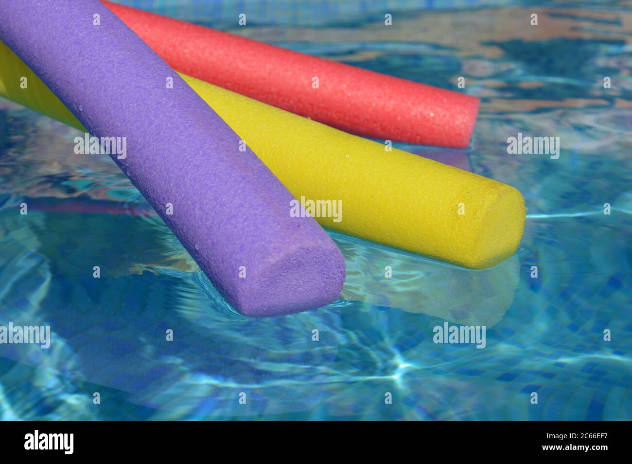 Nouilles de bain aux couleurs vives, pourpres, jaunes et rouges, flottant sur l'eau d'une piscine carrelée de bleu, Banque D'Images