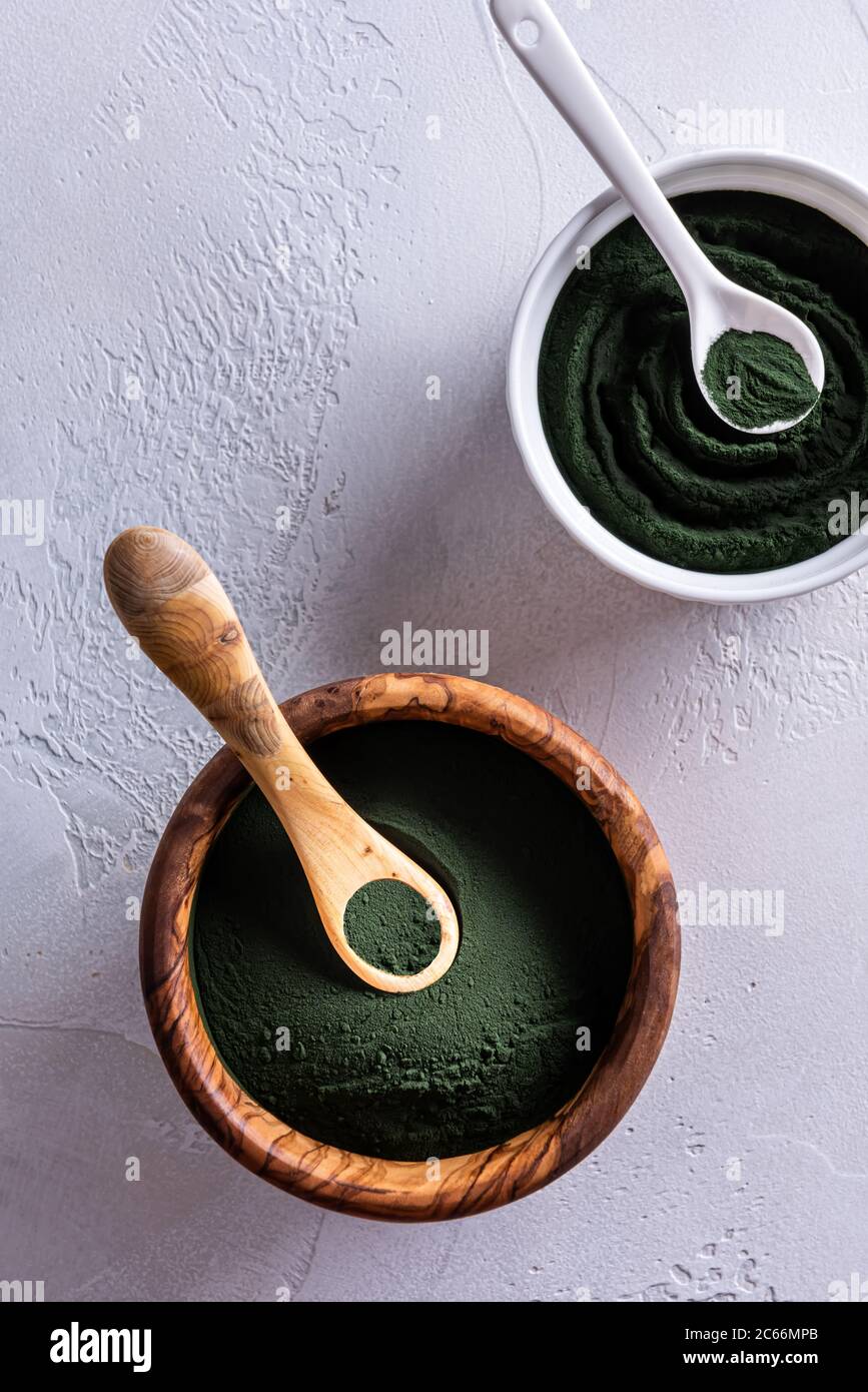 Poudre de chlorelle ou de spiruline dans un bol en bois et dans un bol en porcelaine par le dessus. Les bols sont dotés de cuillères assorties. Alimentation saine et diétine Banque D'Images