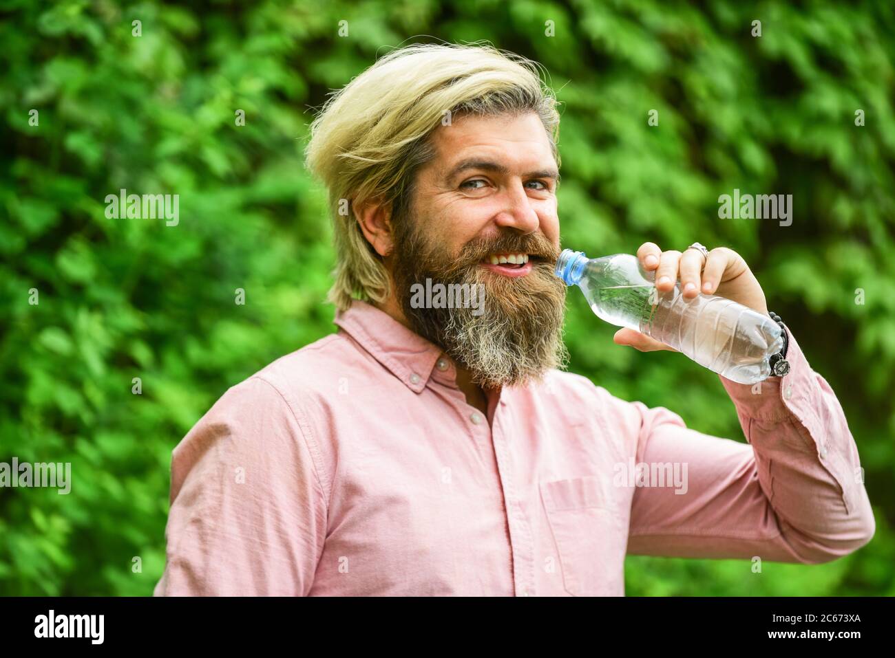 il faut boire un verre. un homme brutal boit de l'eau. un homme barbu tient une bouteille d'eau en plastique. il a soif. buvez un peu d'eau en marchant dans le parc. rafraîchissez-vous. Maintenir l'équilibre de l'eau dans le corps. Banque D'Images