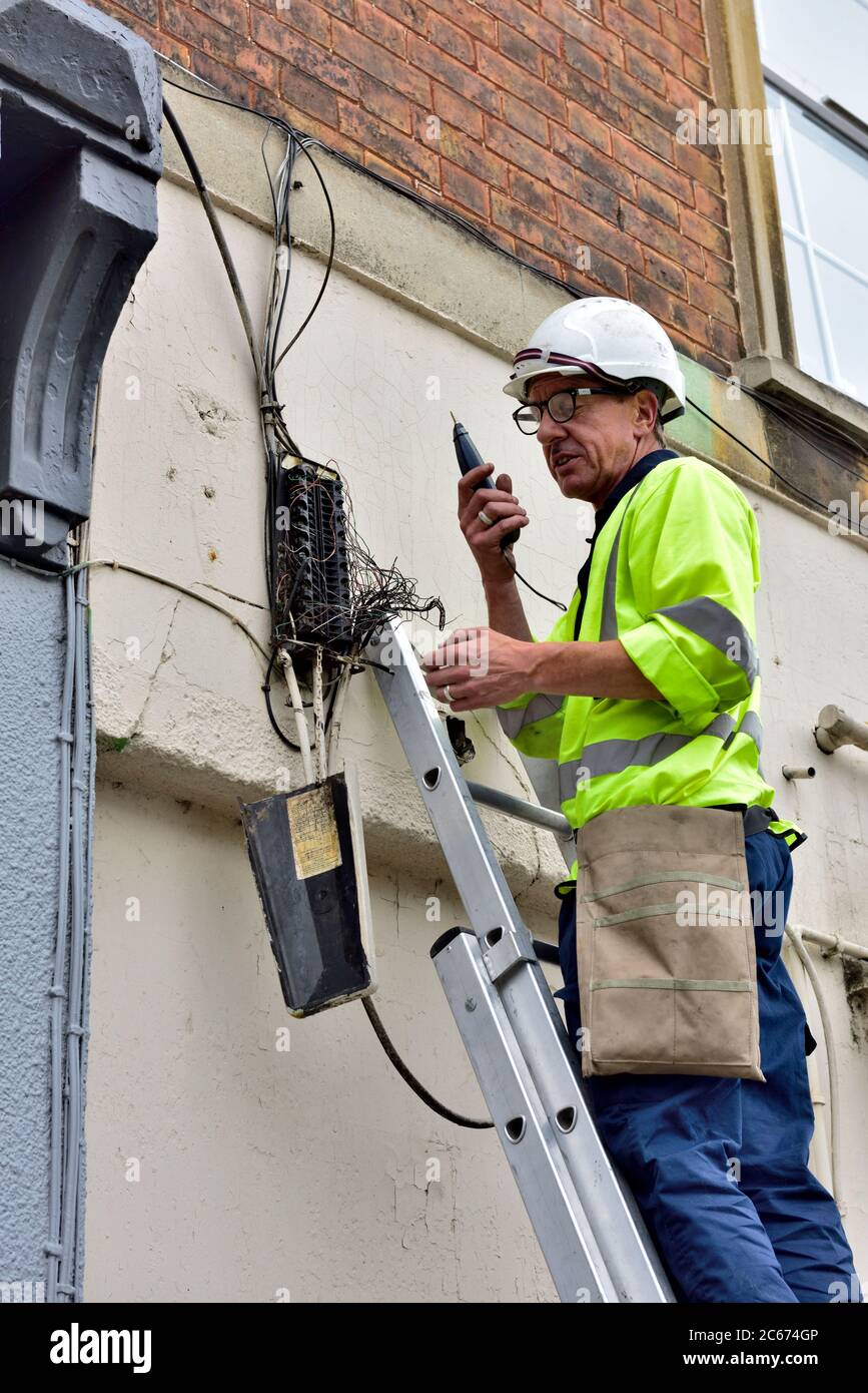 Ingénieur téléphonique sur une échelle avec générateur de tonalités testant un nid de fils de cuivre pour tracer une connexion dans le boîtier de raccordement de la maison Banque D'Images