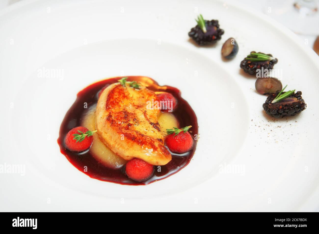 Foie de canard frit avec sauce au vin et baies dans une assiette de porcelaine blanche, tonifiée Banque D'Images