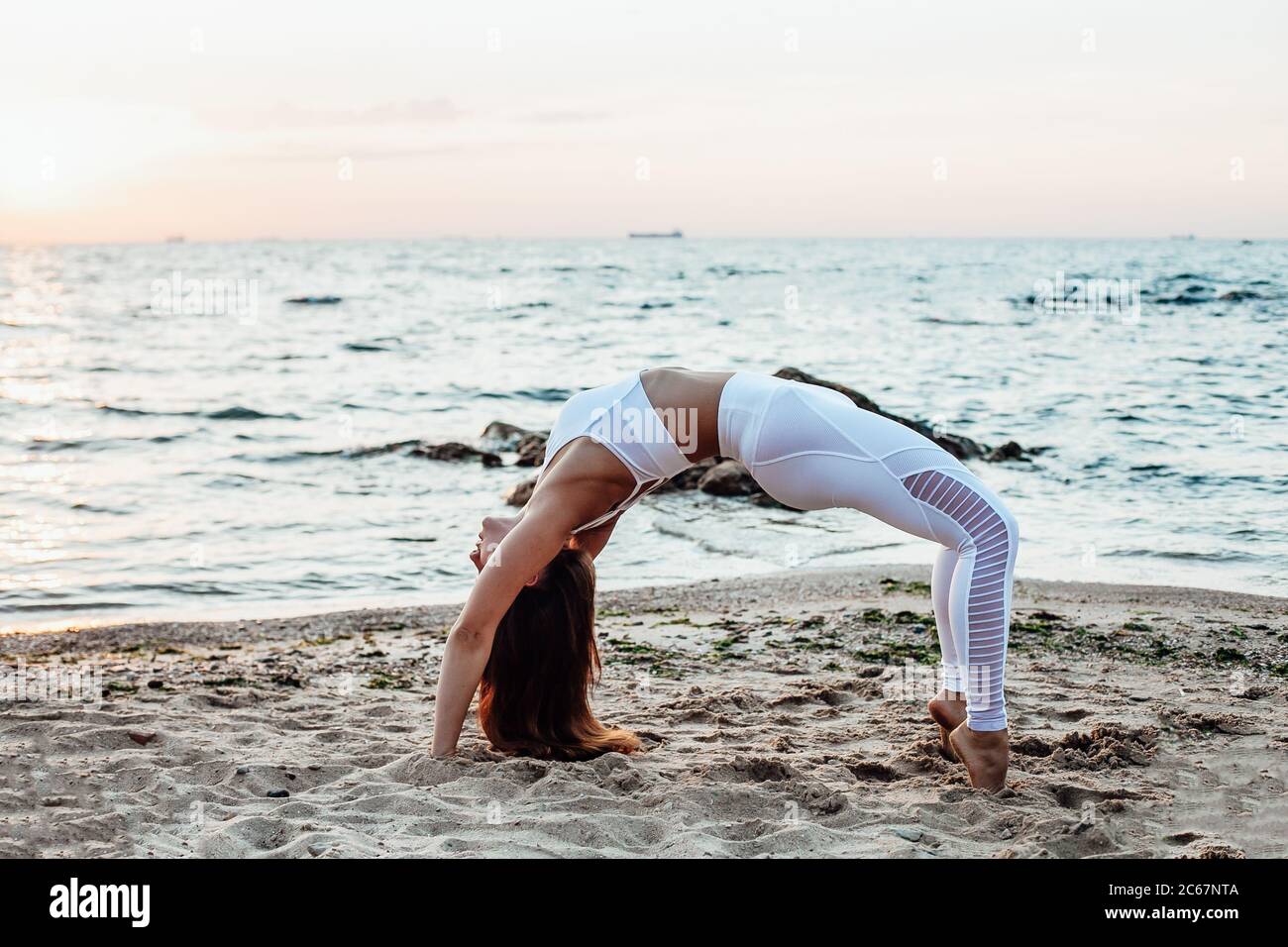 Vue latérale d'une jeune femme debout dans un poste de yoga Warrior sur une plage de sable Banque D'Images