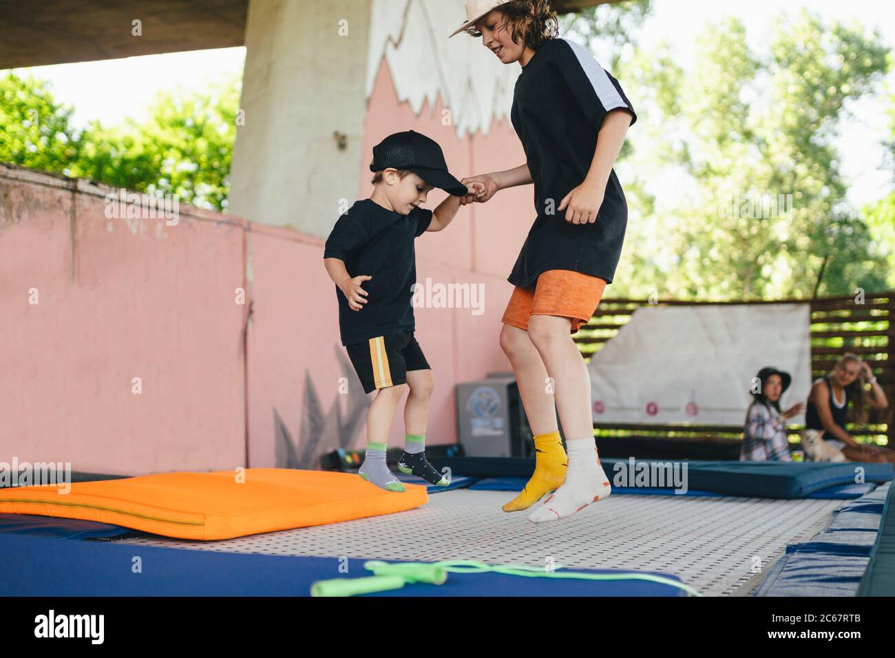 Le grand frère enseigne aux jeunes à sauter sur un trampoline. Enfants en activité de loisir trampoling tenant les mains ensemble. Week-end sportif au centre sportif Banque D'Images