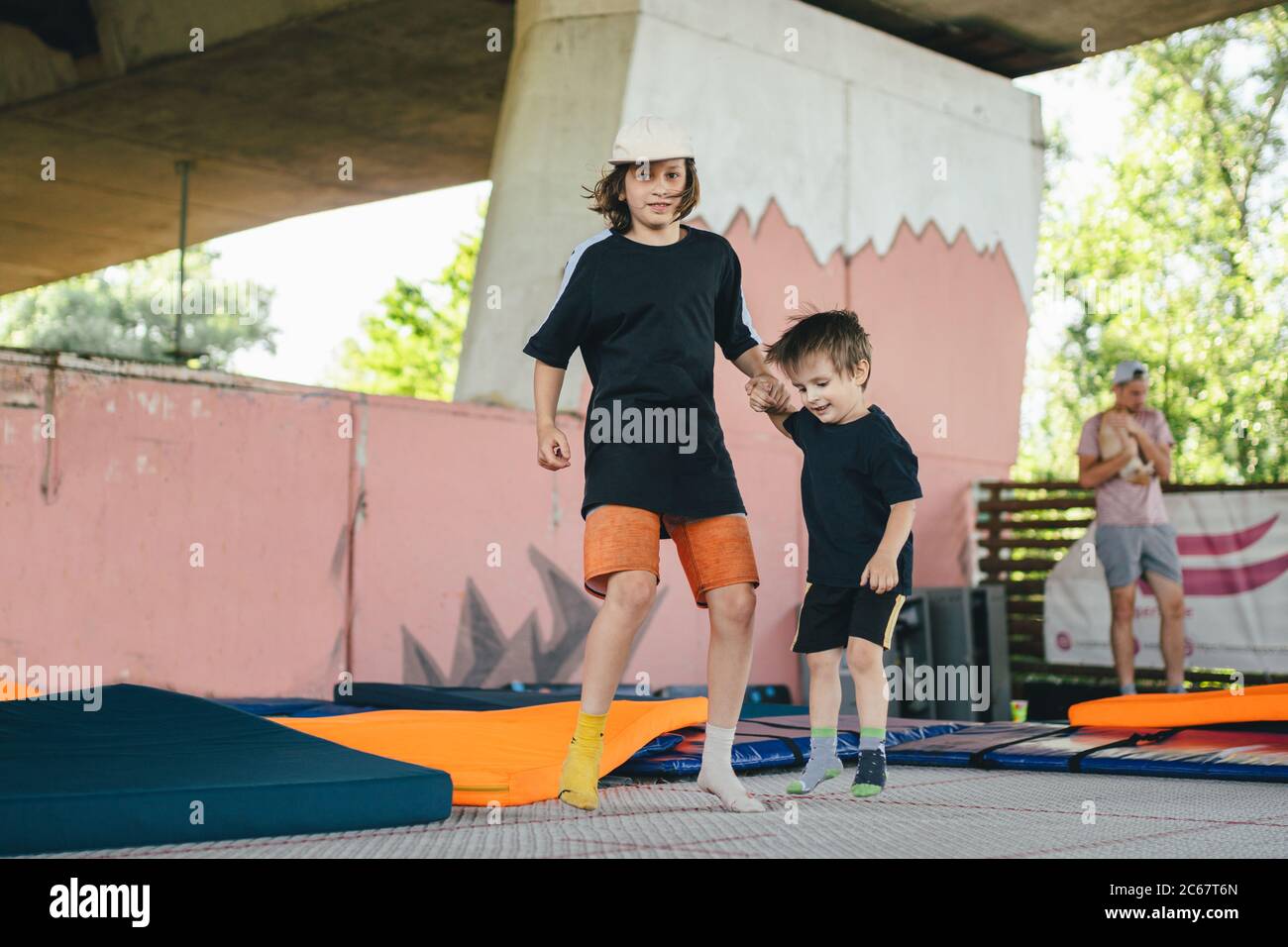 Le grand frère enseigne aux jeunes à sauter sur un trampoline. Enfants en activité de loisir trampoling tenant les mains ensemble. Week-end sportif au centre sportif Banque D'Images