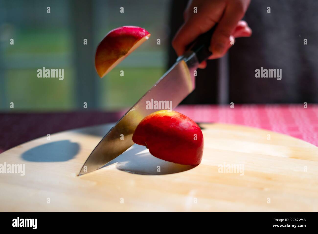 Gros plan du chef hacher la pomme à la main en deux avec un couteau de cuisine sur la table. Trancher la pomme rouge sur un panneau en bois Banque D'Images