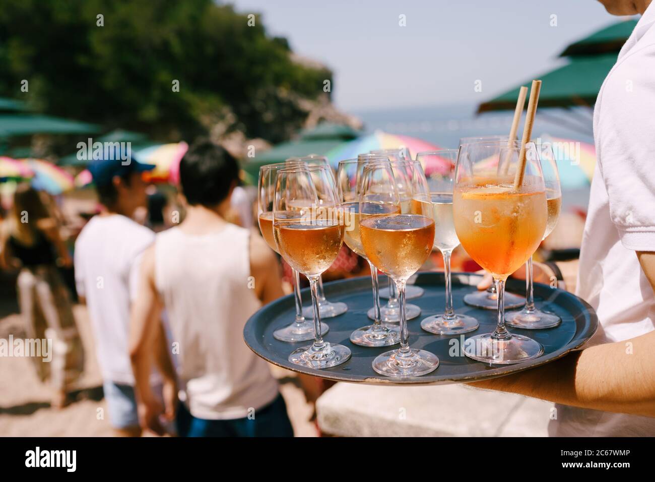 Un serveur avec un plateau à la main propose des cocktails et des boissons lors d'une fête sur la plage - un cocktail d'orange dans un grand verre avec un tube Aperol spritz et Banque D'Images