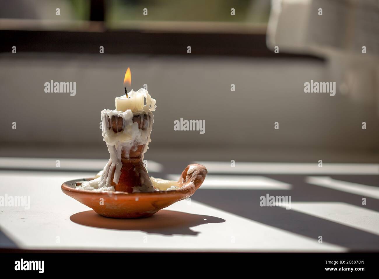 Photographie rapprochée d'une bougie brûlante dans un chandelier en argile fait main près d'une fenêtre ensoleillée Banque D'Images