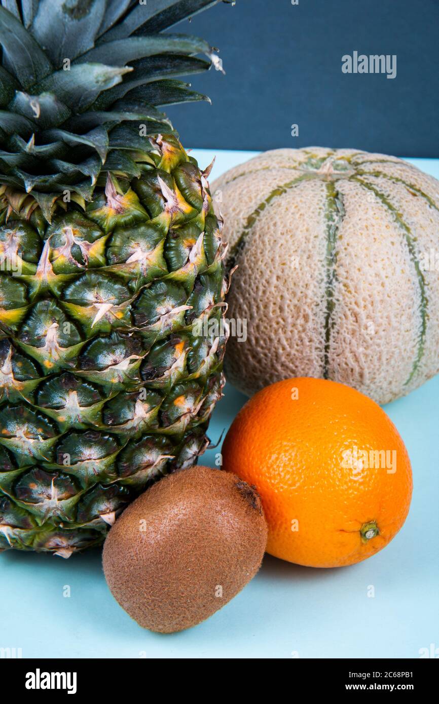 Un ananas, un melon de miel, de l'orange et du kiwi sur une surface bleue. Banque D'Images