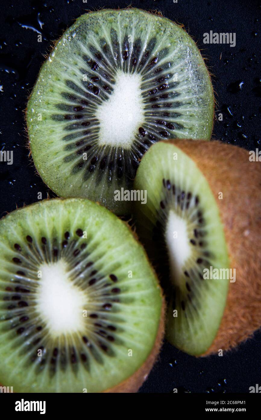 Un gros plan de quelques tranches de kiwis fraîches sur un fond noir humide. Banque D'Images