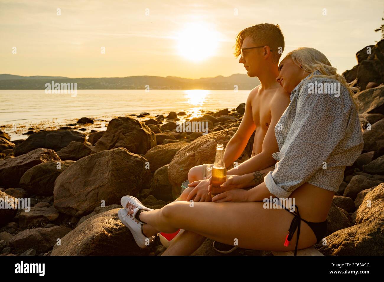 Couple et de boire une bière sur la plage au coucher du soleil Banque D'Images