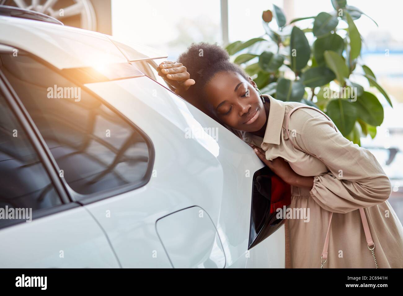 belle femme afro rêve de nouvelle voiture, jeune femme est venue voir des automobiles, faire l'achat. femme est penchée sur la voiture blanche luxueuse, souriant Banque D'Images