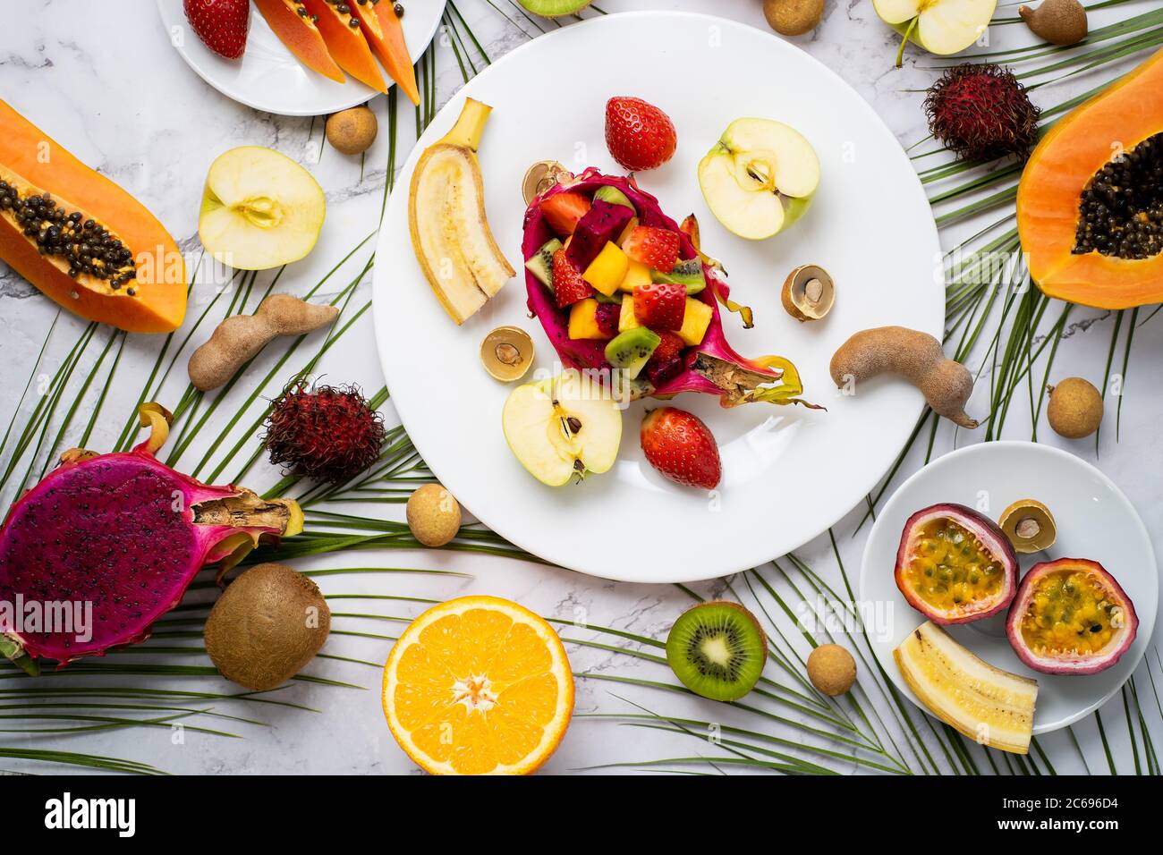 Vue de dessus des assiettes avec des fruits tranchés. Assortiment de différents fruits exotiques avec des feuilles tropicales sur fond de marbre. Délicieux en-cas, vitamine healt Banque D'Images