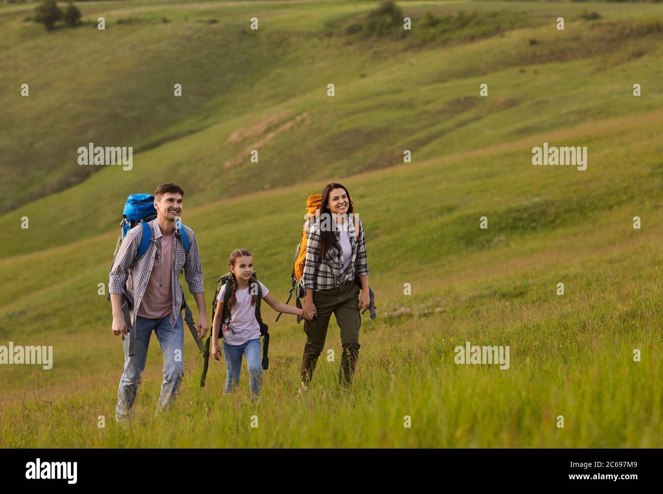 Une famille de touristes rangeant des ckpack est en marche le long de l'herbe sur une colline dans les montagnes. Banque D'Images