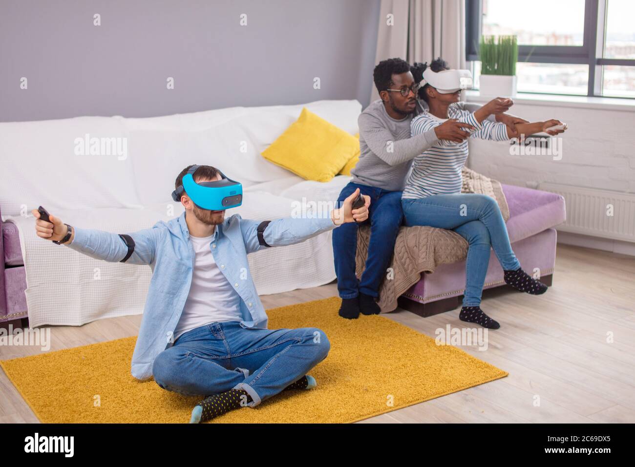 Groupe d'amis multucultural s'amusant à la maison les jeux en 3D à l'aide de jeu réalité vitrual hi-tech viewer pour les jeux. L'accent sur caucasian man in blue virt Banque D'Images