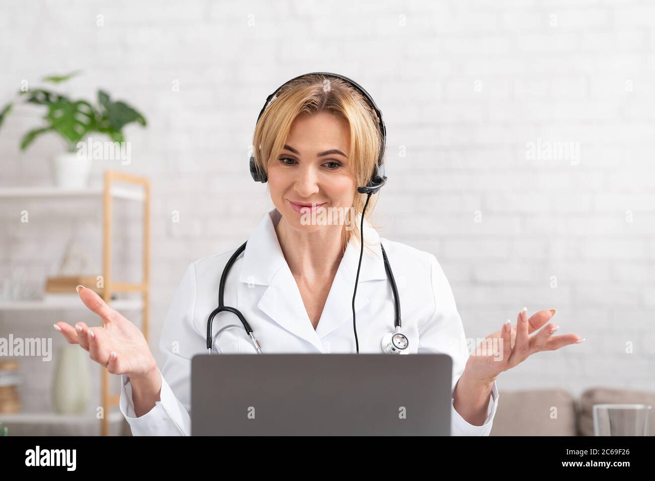 Conférence en ligne avec thérapeute. Une femme médecin la répand sur les côtés et regarde l'ordinateur portable Banque D'Images