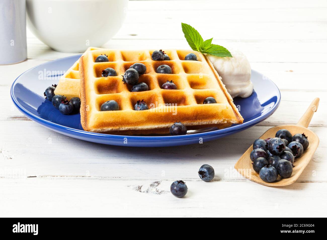 Gaufres belges avec myrtilles et glace à la vanille sur plaque bleue, fruits de rechange sur pelle en bois, table rustique Banque D'Images