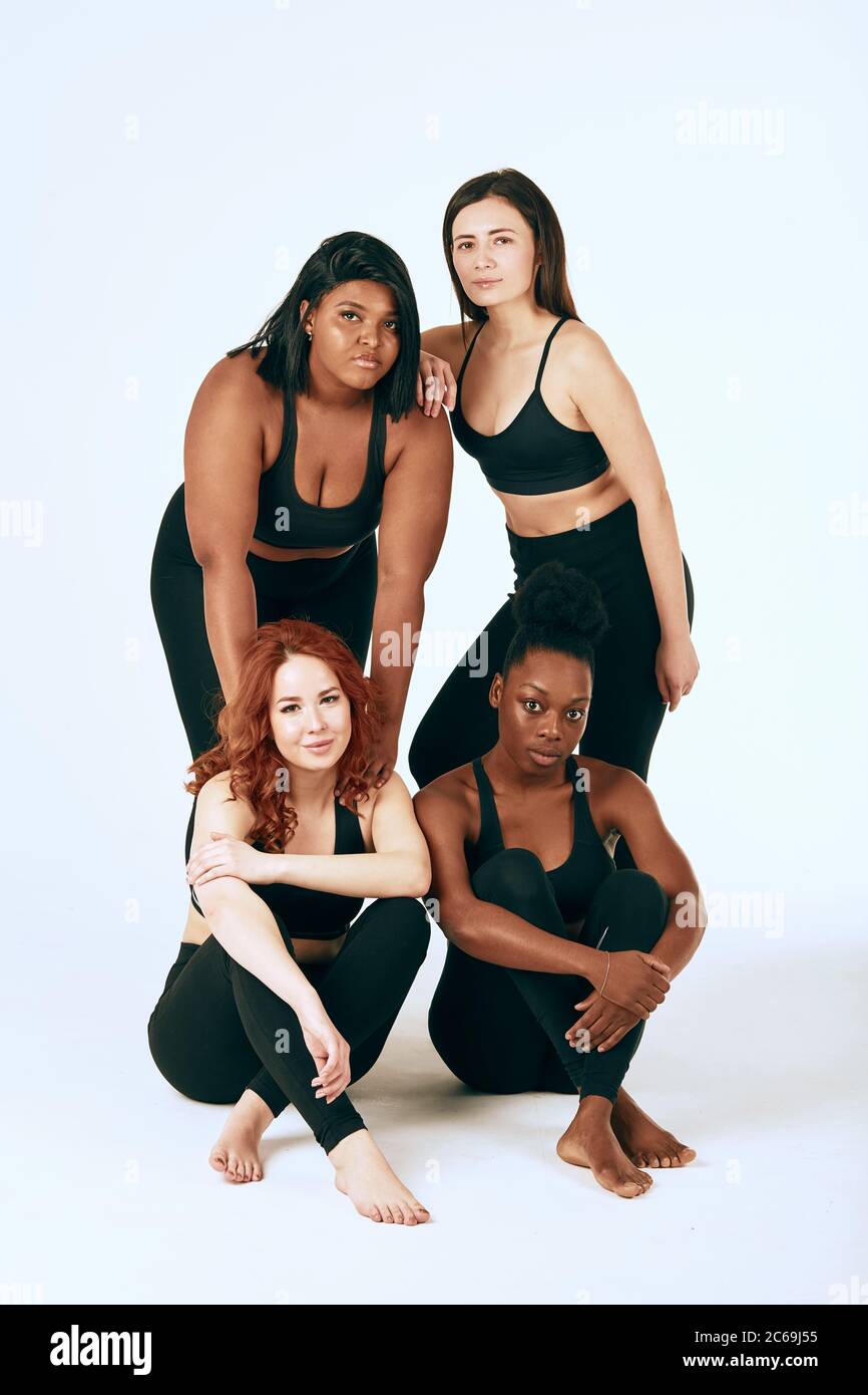 Groupe de quatre femmes de race, de type et de taille différents dans une tenue de sport se posant ensemble sur fond blanc. Banque D'Images