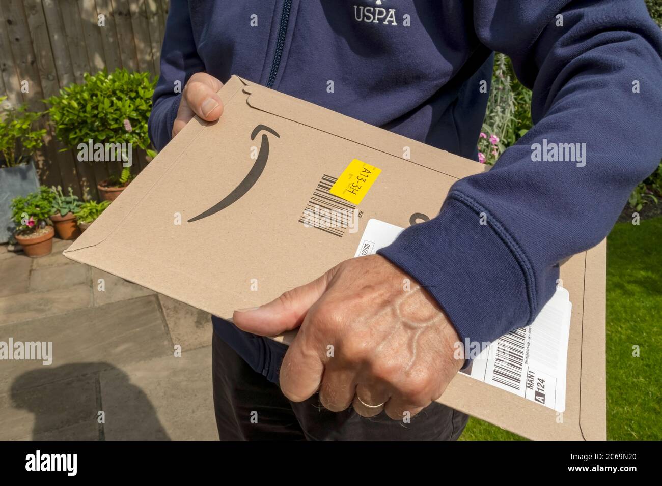 Gros plan de livreur homme personne tenant livraison Amazon paquet paquet colis maison achats Internet Angleterre Royaume-Uni Grande-Bretagne Banque D'Images