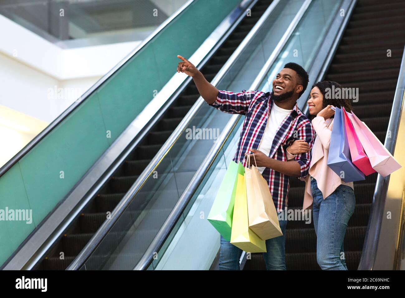 Concept de vente. Un couple noir heureux avec des sacs de shopping sur l'escalier roulant Banque D'Images