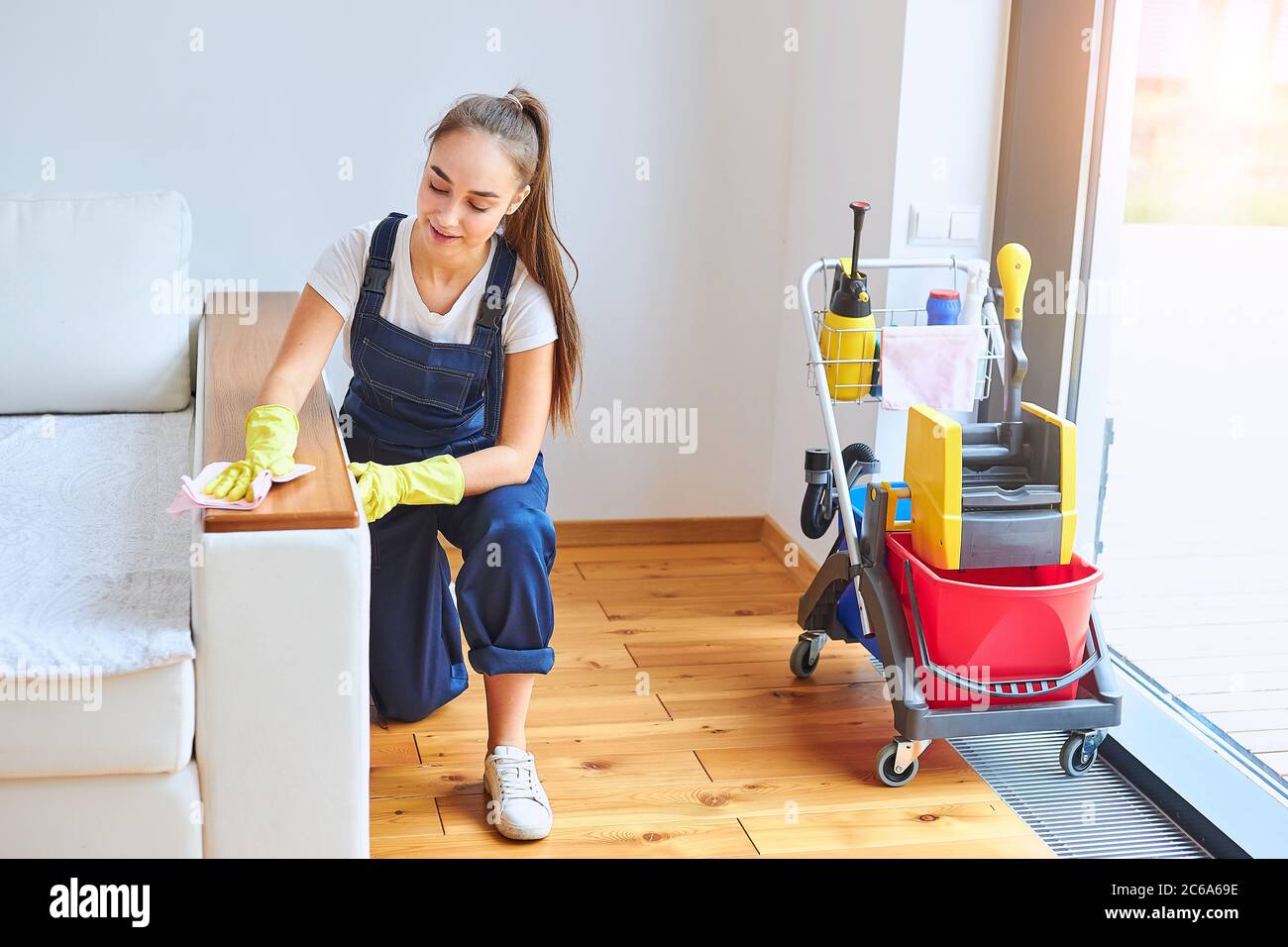 Jeune femme en uniforme de nettoyage faisant du travail dans un nouvel  appartement, en utilisant un chiffon rose pour se laver, profiter du  nettoyage. Concept de service de nettoyage, personnel, travail Photo