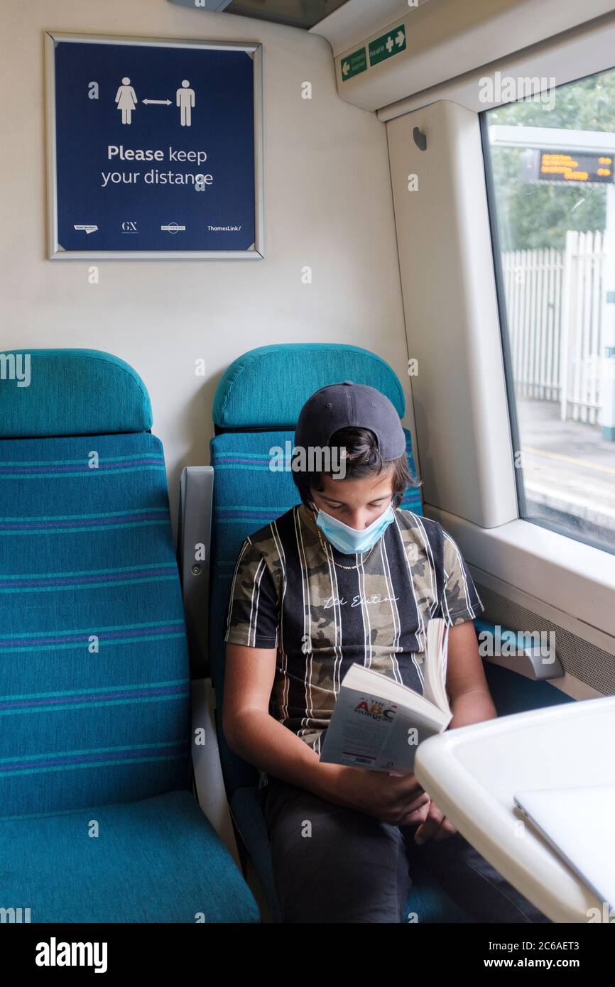 Garçon lit sur le train portant un masque facial, Londres, Royaume-Uni Banque D'Images