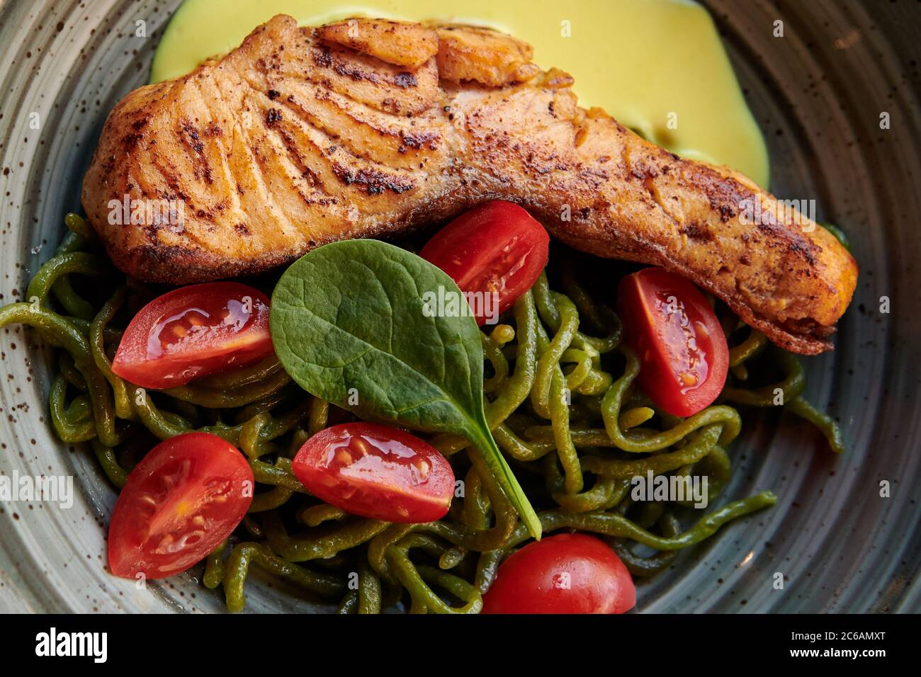 Steak de saumon avec pâtes vertes, tomates cerises et sauce au fromage dans l'assiette vintage. Un plat sain avec du poisson rouge au restaurant. Gros plan. Banque D'Images