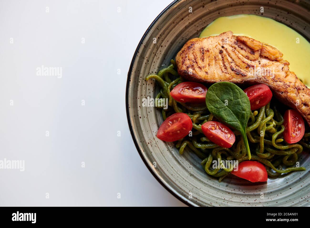 Steak de saumon avec pâtes vertes, tomates cerises et sauce au fromage. Un plat sain avec du poisson rouge au restaurant. Arrière-plan blanc avec espace de copie. Banque D'Images