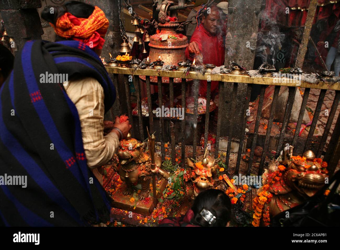 Grand prêtre photographié à côté du grand ghanta (cloche rituelle hindoue) et lampes à huile rituelles dans le sanctuaire principal du temple Dakshinkali près de Katmandou, Népal. Un des temples hindous majeurs du Népal dédié à la déesse Kali est connu pour ses sacrifices animaux qui ont lieu dans le sanctuaire principal. Banque D'Images