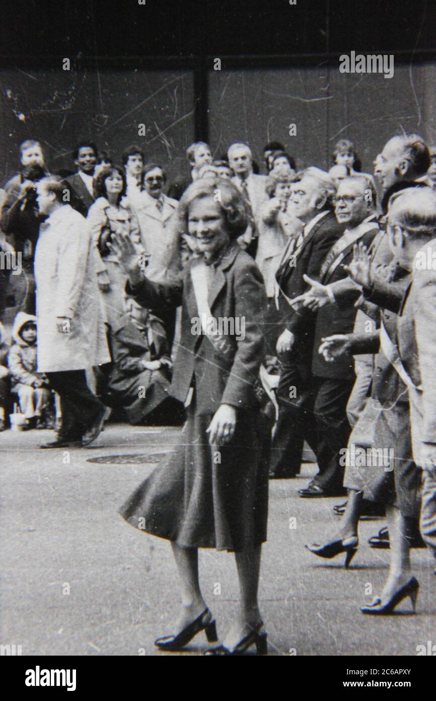 Belle photo de style de vie noir et blanc vintage des années 70 d'une femme qui marche à travers le défilé comme une célébrité locale. Banque D'Images