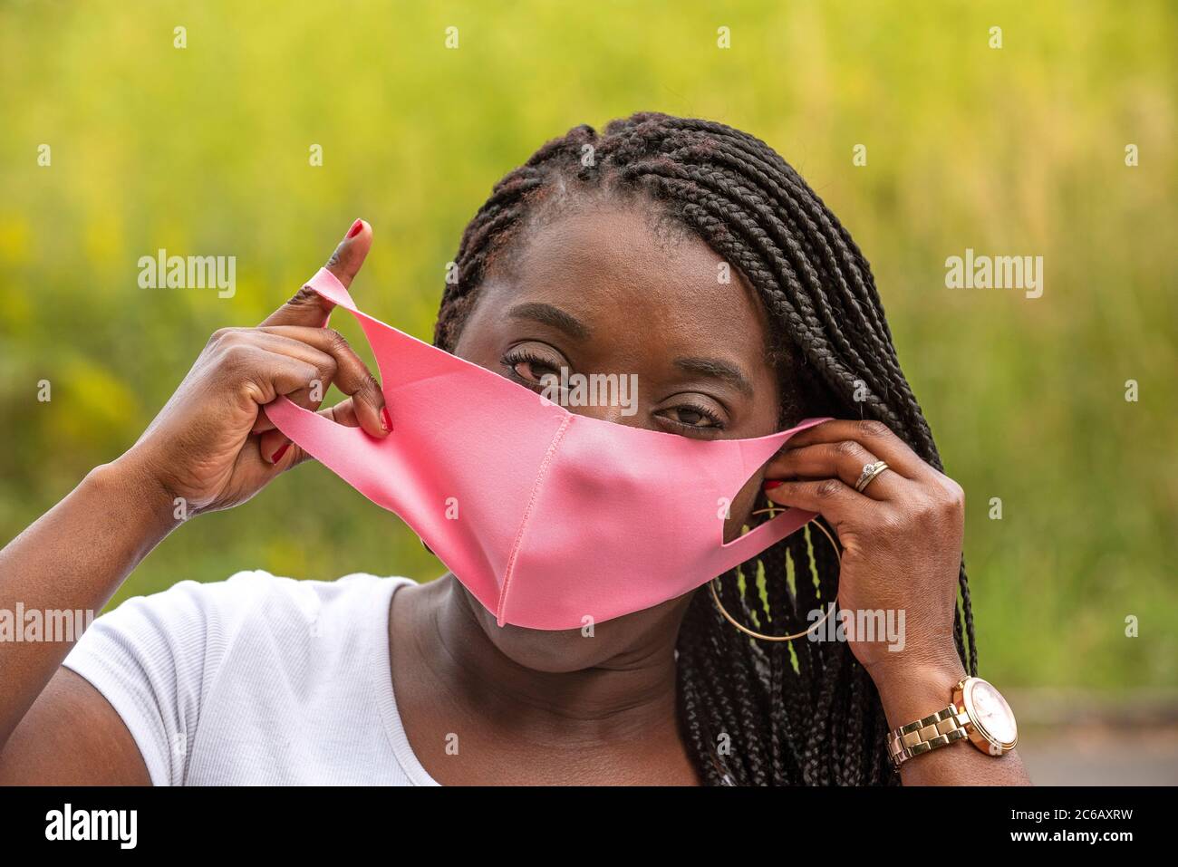 Angleterre, Royaume-Uni. 2020. Portrait d'une femme noire avec un style de cheveux tressé et portant un masque rose pendant l'épidémie de Covid-19 Banque D'Images