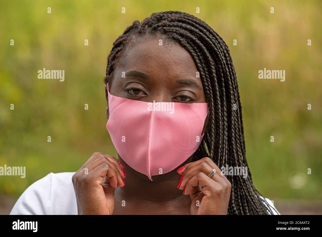 Angleterre, Royaume-Uni. 2020. Portrait d'une femme noire avec un style de cheveux tressé et portant un masque rose pendant l'épidémie de Covid-19 Banque D'Images