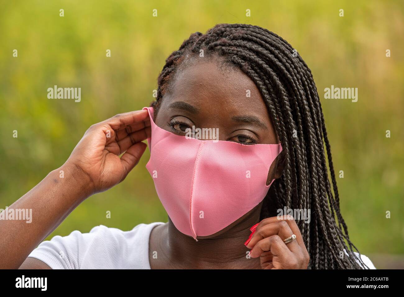 Angleterre, Royaume-Uni. 2020. Portrait d'une femme noire avec un style de cheveux tressé et portant un masque rose pendant l'épidémie de Covid-19 Banque D'Images