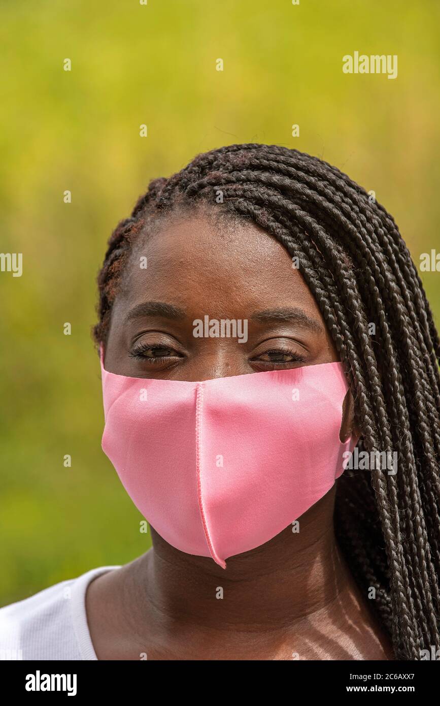 Angleterre, Royaume-Uni. 2020. Portrait d'une femme noire avec un style de cheveux tressé et portant un masque rose pendant l'épidémie de Covid-19 Banque D'Images
